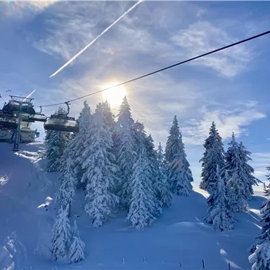 Eine malerische Winterlandschaft mit schneebedeckten Bäumen und einem Skilift. Die Sonne scheint über die schneereichen Hügel.