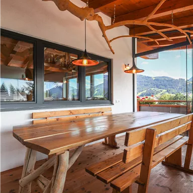 A cozy dining area with a large wooden table and benches. The windows provide a beautiful view of the mountains.