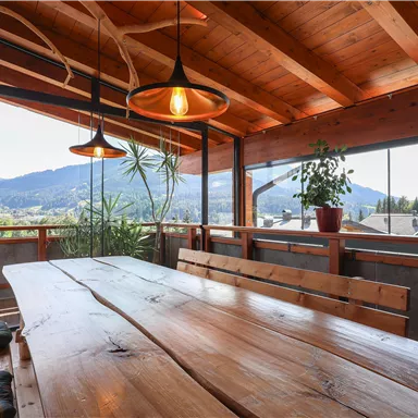 An inviting dining area with a large wooden table and warm wood details. Through the window, one looks out onto a picturesque mountain landscape.