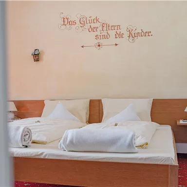 A cozy bedroom with two beds and fresh towels. An inspiring quote about the happiness of parents and children is on the wall.