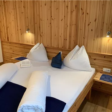 A cozy bedroom with wooden paneling and a large double bed. There are comfortable cushions and decorative elements on the nightstands.