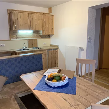 A cozy kitchen unit with wooden shelves and a dining table. On the table, there is a fruit bowl and a blue table runner.