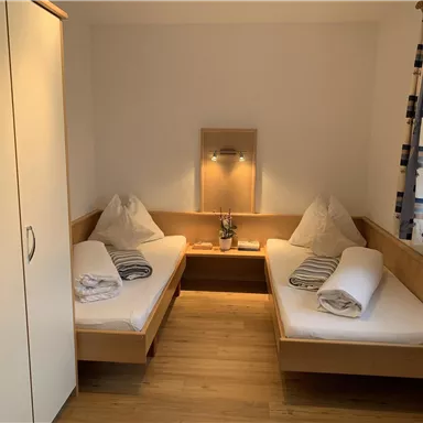 A cozy room with two single beds and wooden furniture. There is a wardrobe and pleasant lighting.