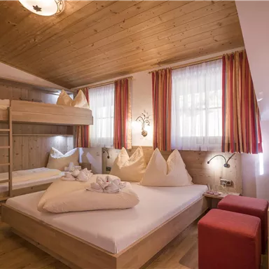 A cozy room with wooden decor and light curtains. There is a double bed, a loft bed, and a comfy seating area.