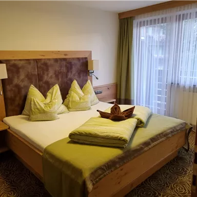 Ein gemütliches Schlafzimmer mit einem großen Bett und dekorativen Kissen. Der Raum hat viel natürliches Licht und eine ruhige Atmosphäre.