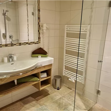 Ein modernes Bad mit einer eleganten Waschbeckenanlage und Spiegelschränken. Die Dusche ist durch eine Glaswand abgetrennt, und ein Handtuchheizkörper ist ebenfalls vorhanden.
