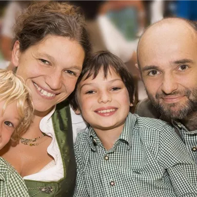 A family poses happily in traditional clothing. They smile at the camera and seem to be having a wonderful time together.