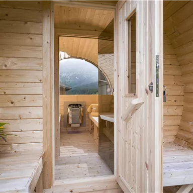 A cozy wooden cabin entrance with a beautiful view of nature. Inside, there is a table and a cooking facility.