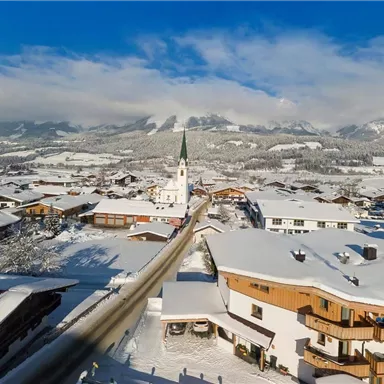 A picturesque village in winter with snow-covered hills and a church. The clear blue sky contrasts with the white landscape.