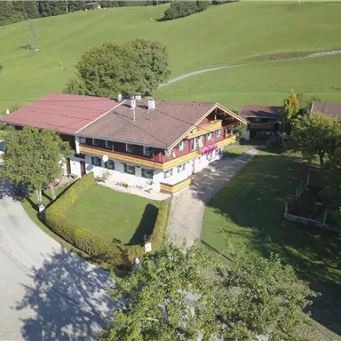 Ein malerisches Haus mit rotem Dach, umgeben von grünen Wiesen und Bäumen. Die Umgebung ist ruhig und einladend.