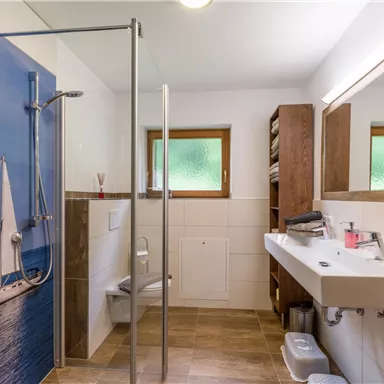 Ein modernes Badezimmer mit einer Dusche und einem großen Spiegel. Der Hintergrund zeigt ein maritimes Motiv mit einem Segelboot.