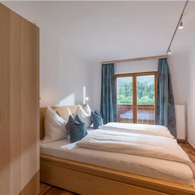 Ein modernes Schlafzimmer mit einem Doppelbett und zwei Kissen. Große Fenster bieten einen Blick ins Grüne und sicheres Licht.