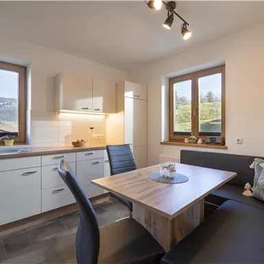 A modern kitchen with a window and a cozy dining area. The furniture is in bright colors and there is a beautiful view of the surrounding landscape.