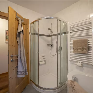A modern bathroom with a glass shower enclosure and a wooden cabinet. The walls are light tiled and a towel rack is available.
