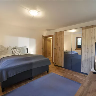 A modern bedroom with a large bed and wooden furniture. The room is bright and inviting, with a television and a large wardrobe.