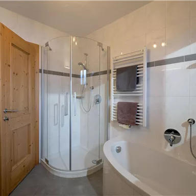 A modern bathroom with a shower cubicle and a bathtub. The walls are brightly tiled and there is a towel warmer.
