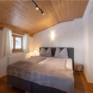 A cozy bedroom with a double bed and bright wooden ceiling. The windows let in a lot of light and create a relaxed atmosphere.