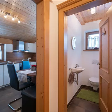A cozy interior with a modern kitchen and an adjoining bathroom. Wooden paneling and large windows create a bright, inviting atmosphere.