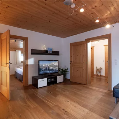A beautiful living space with a wooden ceiling and warm tones. There is a television, a coffee table, and access to other rooms.