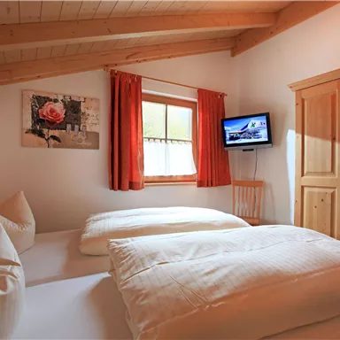 A cozy bedroom with two beds and orange curtains. A picture is hanging on the wall, and a television is available.