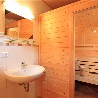 A clean bathroom with a sink and a wooden sauna in the background. The walls are made of light wood, creating a warm atmosphere.