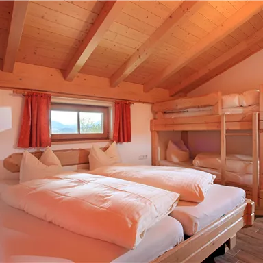 A cozy sleeping room with two single beds and a loft bed. The room has wooden walls and large windows with a view.