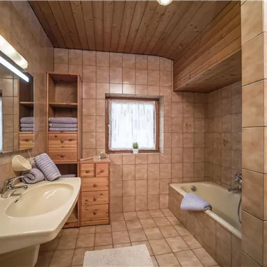 Ein modernes Badezimmer mit gefliesten Wänden und einem großen Fenster. Es gibt eine Badewanne, ein Waschbecken und funktionale Regale.