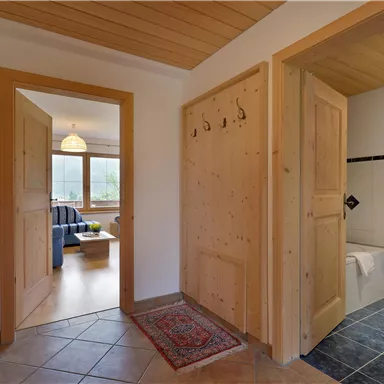 A spacious hallway with wood paneling and a carpet. On the right side is a bathroom, and in the background, you can see a cozy living room.