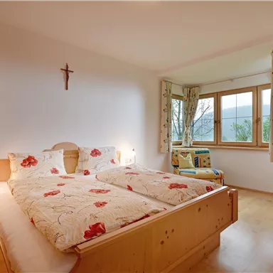 A cozy bedroom with a double bed and wooden shelves. The room has a window with a view to the outside and soft light.