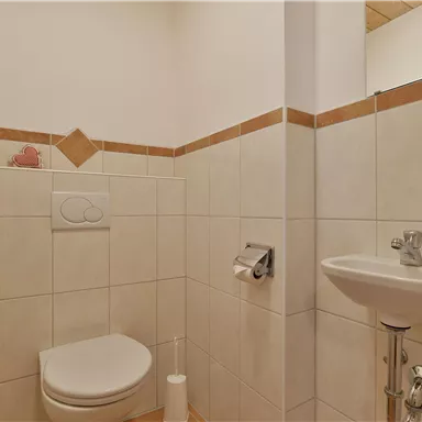 A small bathroom with a toilet and a sink. The walls are tiled in light colors with decorative tiles.