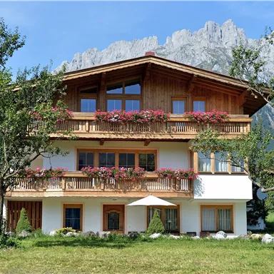 A charming alpine house with balconies and floral decorations. Impressive mountains can be seen in the background.