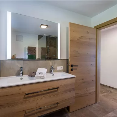 A modern bathroom with a wooden sink and a large mirror. There is a glass shower and a bright, friendly atmosphere.