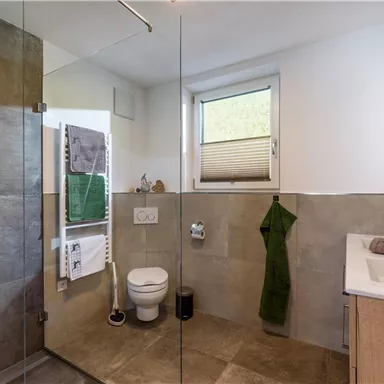 A modern bathroom with a glass shower and elegant tiles. It features a sink and towels in neutral colors.