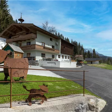 A rustic building in the middle of a forest, surrounded by a green meadow. Decorative metal figures of animals stand in front of the house.