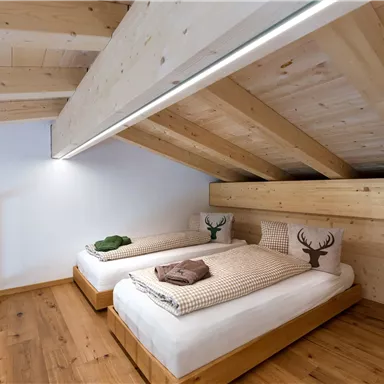 A cozy bedroom with two wooden twin beds. The walls and floor are made of light wood, and there are decorative cushions with a deer motif.