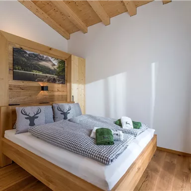 A cozy bedroom with wood decor and two beds. The decoration includes pillows with a deer motif and green towels.