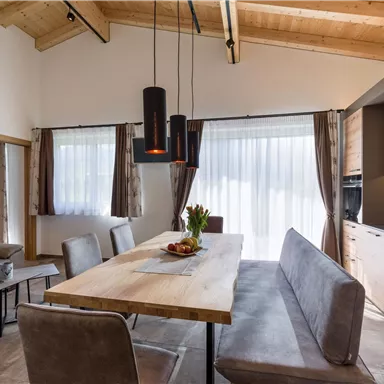 A modern dining room with a large wooden table and comfortable benches. The large windows allow plenty of daylight in, and the wooden ceiling creates a cozy atmosphere.