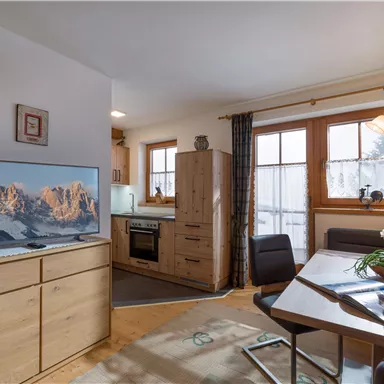 A cozy living space with a modern kitchen and a large window. The room is bright and inviting, featuring a television and a dining table.