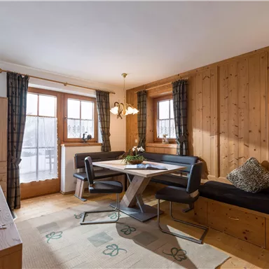A cozy living area with wooden walls and a modern dining table. Large windows provide plenty of light and a pleasant atmosphere.