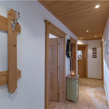 An inviting hallway with wood-paneled walls and a light floor. Decorative elements hang on the wall, while a small dresser stands at the end of the hallway.