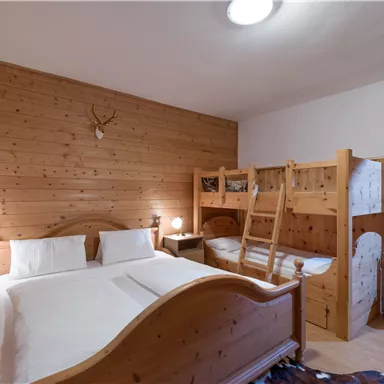 A cozy room with wood paneling and a double bed. There is a bunk bed and a bright, friendly atmosphere.