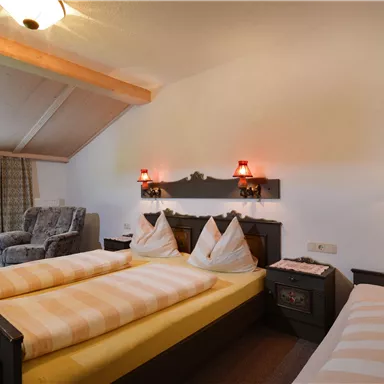 Ein gemütliches Schlafzimmer mit zwei Einzelbetten und traditionellen Kissen. Es gibt einen Sessel und gemütliche Beleuchtung.