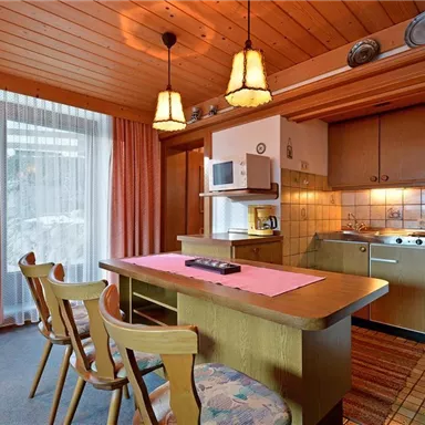 Eine gemütliche Küche mit Holzdecke und einem Esstisch. Die Ausstattung umfasst einen Kühlschrank, eine Mikrowelle und eine Kochstelle.