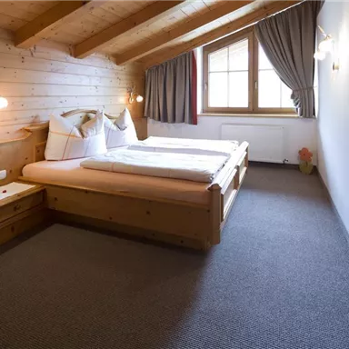 Ein gemütliches Schlafzimmer mit Holzverkleidung. Zwei Betten stehen nebeneinander, und ein Fenster sorgt für natürliches Licht.