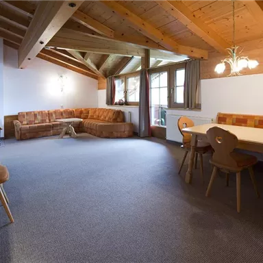 Ein gemütlicher Wohnraum mit Holzdecken und einem großen Fenster. Ein Sofa, ein Esstisch und ein Fernseher sind ebenfalls zu sehen.
