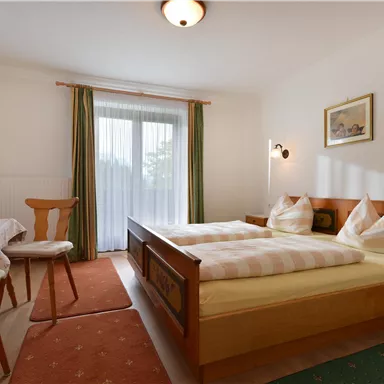 Ein gemütliches Schlafzimmer mit einem Doppelbett und zwei Stühlen. Helle Farben und viel natürliches Licht schaffen eine einladende Atmosphäre.