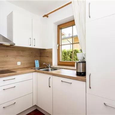 Eine moderne Küche mit weißen Schränken und Holzarbeitsplatte. Das Fenster gibt einen Blick ins Freie und sorgt für viel Tageslicht.