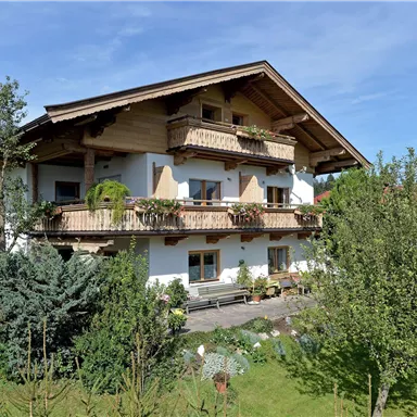 Ein charmantes Landhaus mit verschiedenen Balkonen und vielen Blumen. Umgeben von üppigem Grün und Bäumen ist es einladend und freundlich.