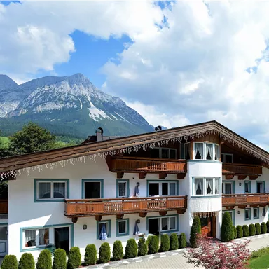 Ein malerisches Gebäude im alpenländischen Stil mit Balkonen und einem schönen Blick auf die Berge. Die Umgebung ist grün und einladend.