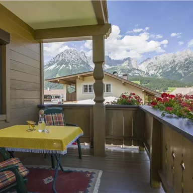 Ein gemütlicher Balkon mit einem gelben Tisch und Blick auf majestätische Berge. Bunte Blumen verschönern die Umgebung und laden zum Entspannen ein.